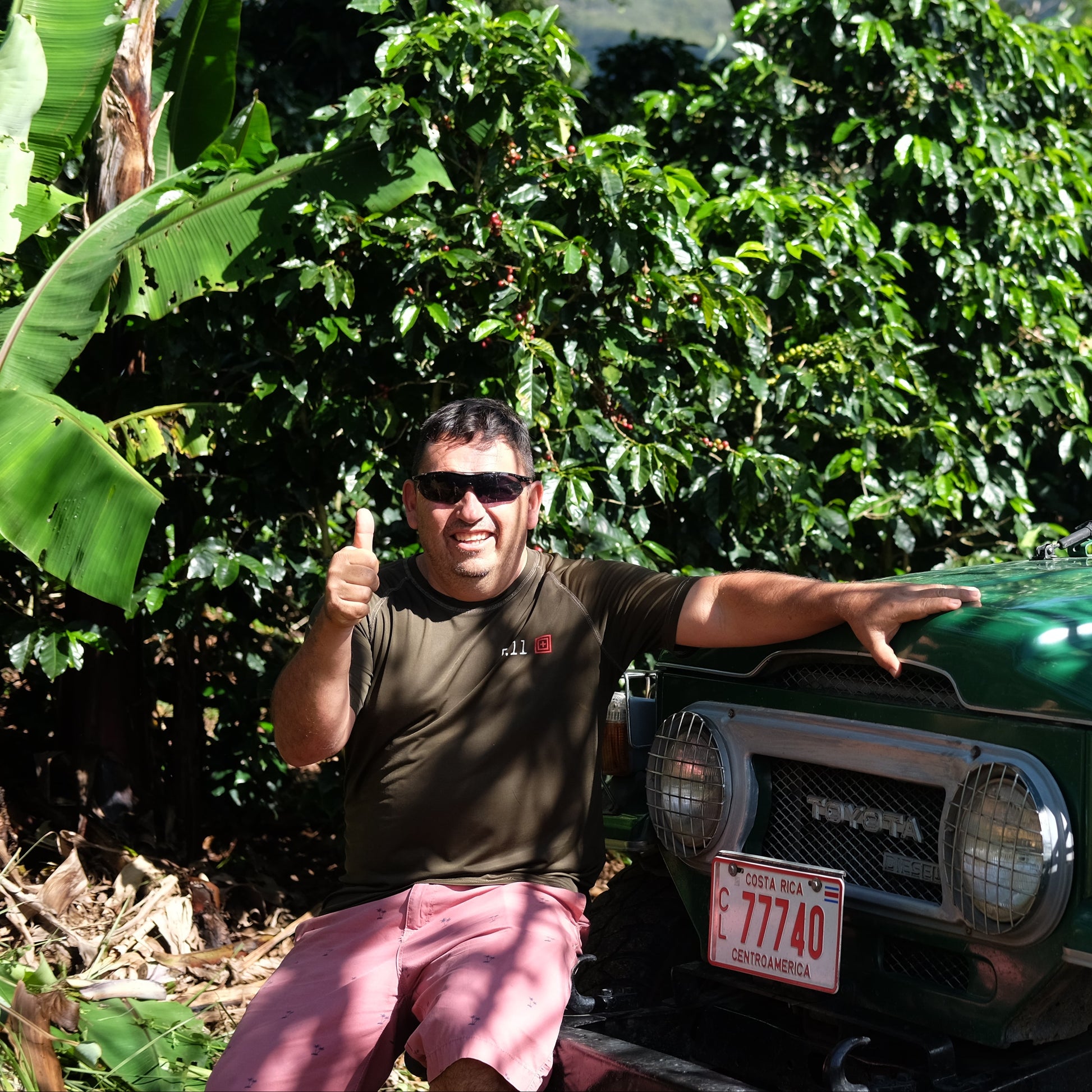 Coffee farmer standing next to a green Toyota Land Cruiser in a coffee plantation