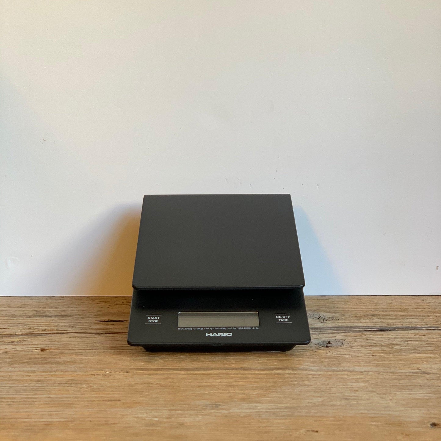HARIO SCALE WITH BUILT IN TIMER SLIGHTLY UPRIGHT ON A WHITE WALL, PLACED ON A WOODEN TABLE (9427968455)