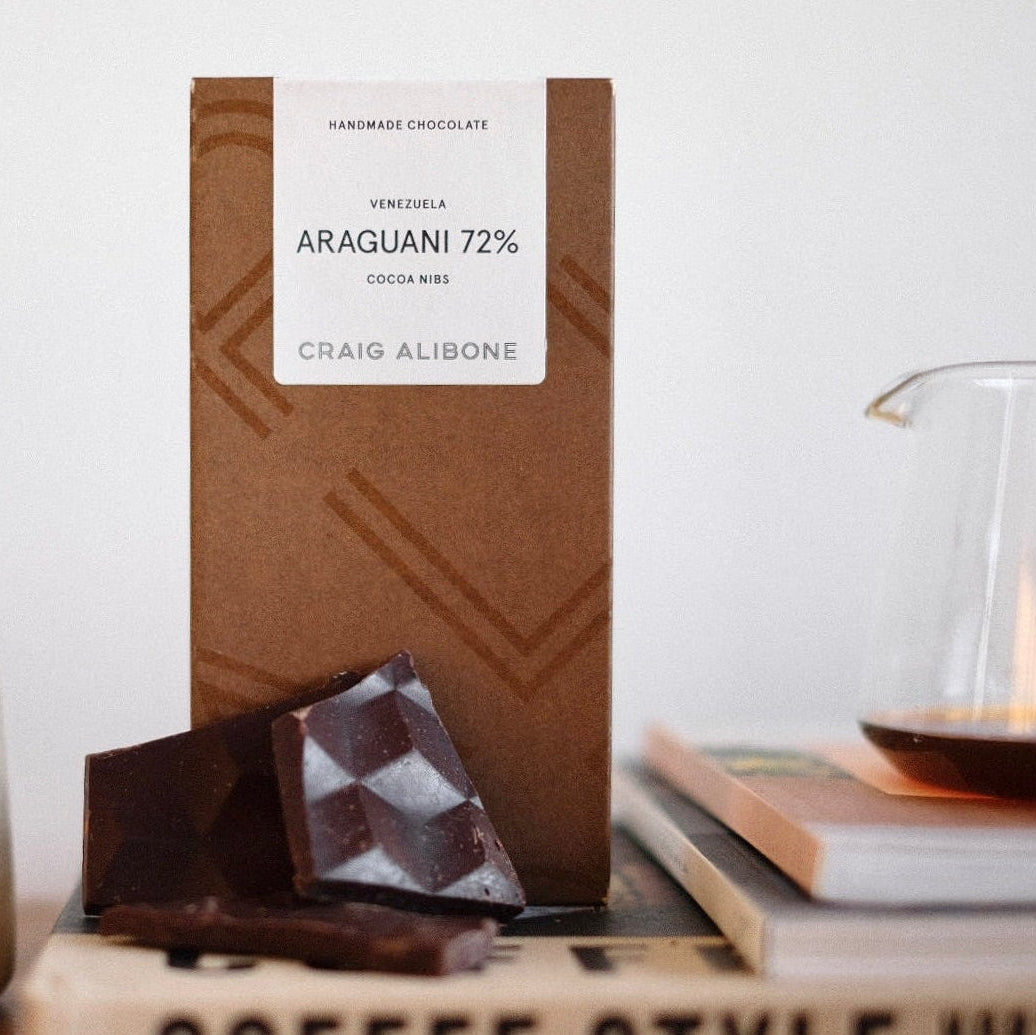 Chocolate bar with a label on a white surface, next to a mug and books.