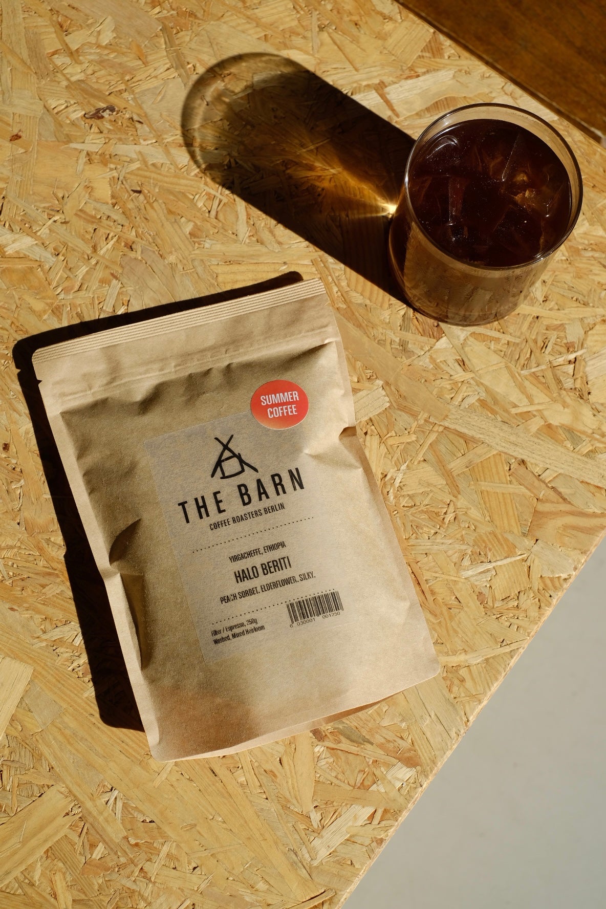 Coffee from Ethiopia package labeled 'The Barn' and an Orange Summer Coffee Sticker on a wooden surface with a glass of coffee.