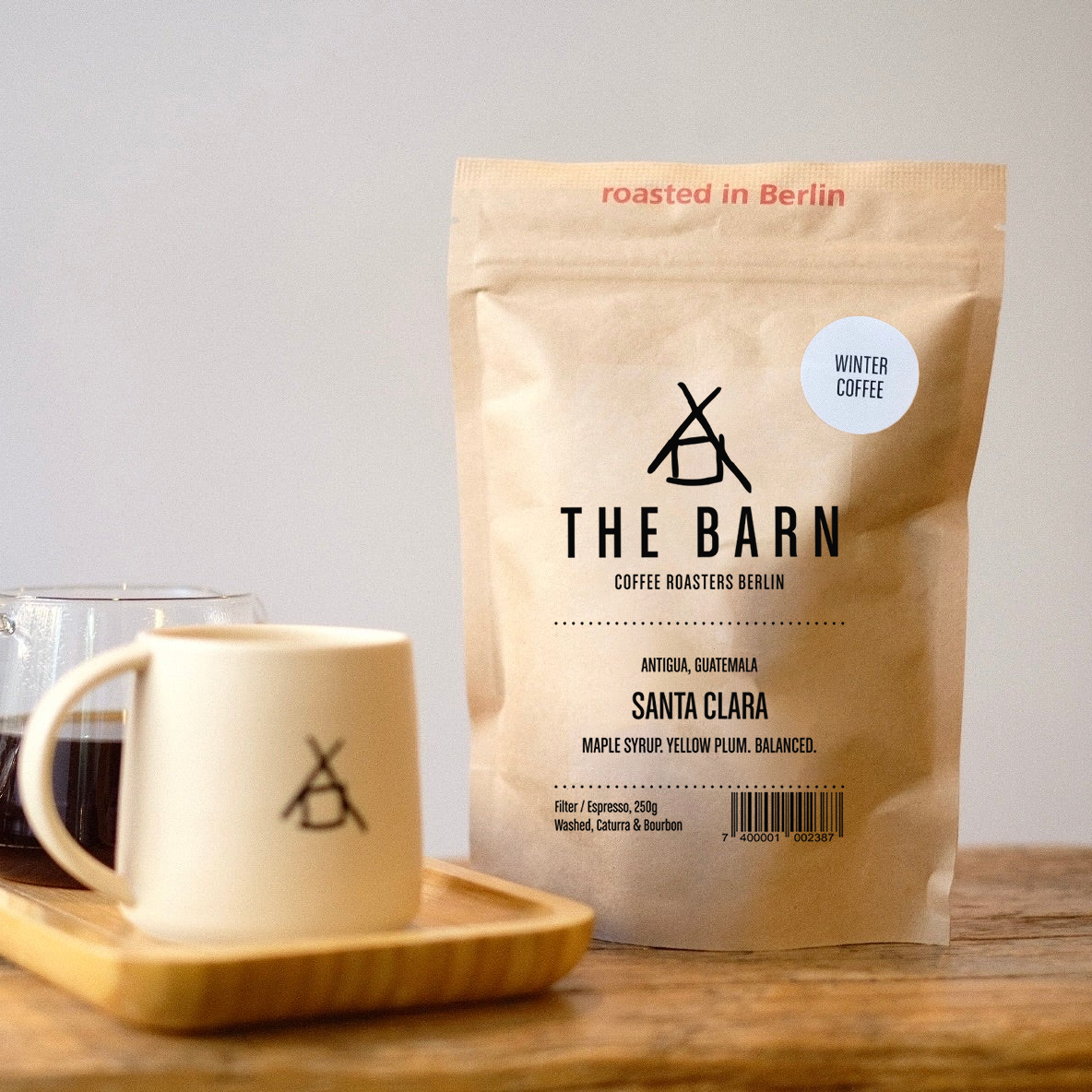Coffee bag and mug with 'The Barn' branding on a wooden surface.