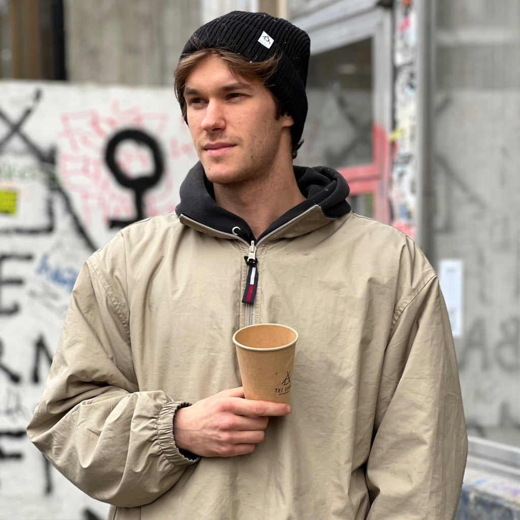 Person wearing THE BARN Coffee Roasters organic vegan cotton beanie in black with a folded cuff and a small tag with the company logo